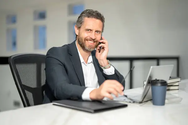 Business talk on phone. Handsome business man working with laptop at desk in office. Businessman typing on keyboard, online business meeting. Businessman working in office. Office worker using laptop
