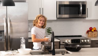 Ev işleri. Mutfaktaki çocuk tabakları temizliyor. Ev mutfağında bulaşık yıkayan tatlı çocuk. Çocuk mutfağın içinde bulaşık yıkıyor. Çocuk anne ve babasına ev işlerinde yardım ediyor