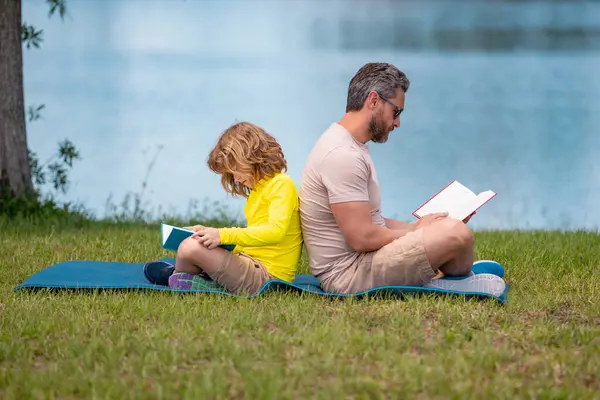 Father and son enjoy spending quality time reading books outdoors. Dad and kid son enjoy nature while reading book outdoors. Father and his little son reading book in park. Fathers day