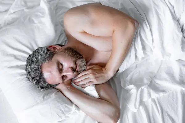 Man sleeping in bed. Top view of handsome man sleeping in bed. Morning healthy sleep. Guy sleeping on bed in bedroom. Middle aged adult man is sleeping at home. Cozy bed, white pillow mattress