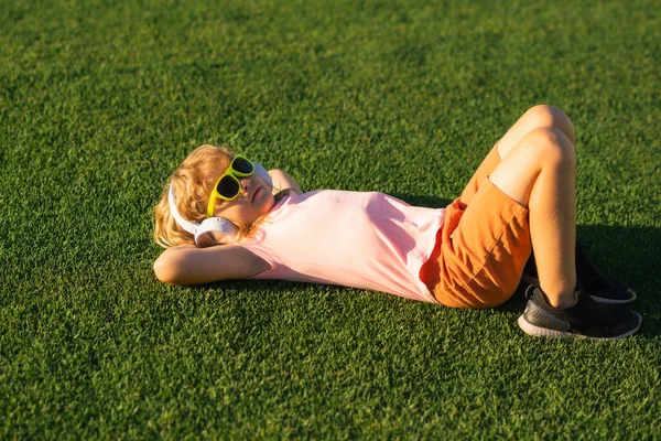 아이들은 헤드폰에 음악을 잔디에 휴식을 있습니다 공원에서 헤드폰에 티셔츠에 감정적 — 스톡 사진