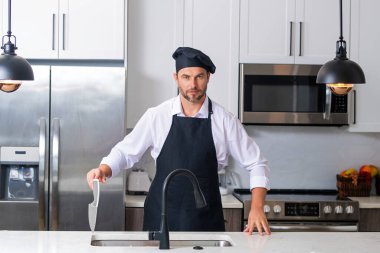 Mutfakta şef üniforması giyen yakışıklı orta yaşlı bir adam. Aşçılık ve aşçılık. Restoran menüsü konsepti. Yemek servisi, yemek pişirme, yemek reklamcılığı. Üniformalı adam mutfakta.