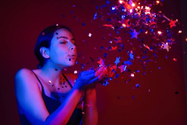 Konfeti üfleyen seksi kız. Doğum gününde, sevgililer gününde güzel bir genç kadının portresi. Seksi kız doğum gününde ışıltı saçar. Doğum gününü kutlayan şehvetli kadın. Sevgililer günün kutlu olsun. Doğum günü partisi