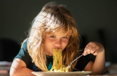Bulanık arka planda yemek yiyen çocuk. Aç küçük çocuk yemek yiyor. Çocuklar için ev yemeği. Lezzetli yemekler, dağınık çocuk spagetti yiyor..