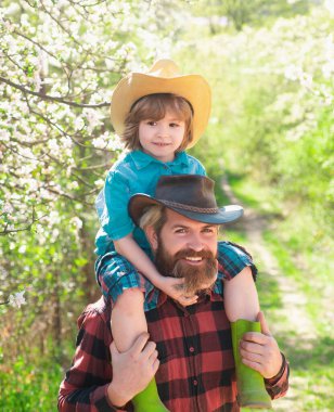 Oğlu babasının omzunda oturuyor. Bahar ailesi güneşli bir günde açık hava parkında ya da bahçede gülümsüyor.