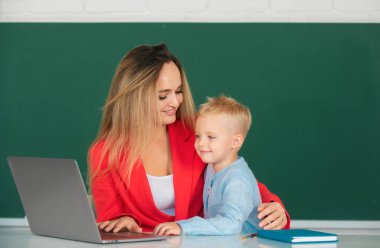 Little school child son using laptop with mother. Elementary school classroom. Teacher and schoolchild pupil in class. Mother and son together using computer laptop