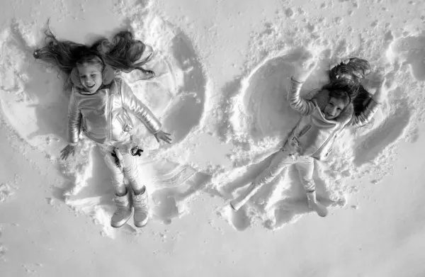 Snow angels made by a kids in the snow. Smiling children lying on snow with copy space. Funny kids making snow angel. Top view