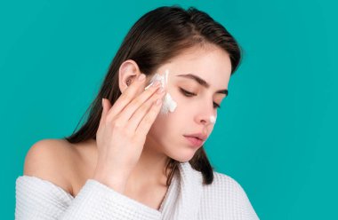 Temiz ciltli güzel bir genç kadın. Güne başlamak için hazırlanan tatlı genç kız yüzüne nemlendirici krem sürüyor.