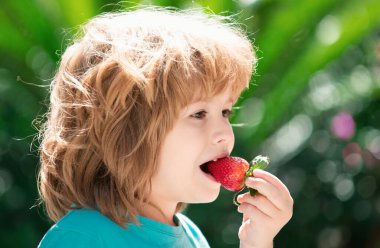 Mutlu çocuk yeşil bahar arka planında çilek yiyor.