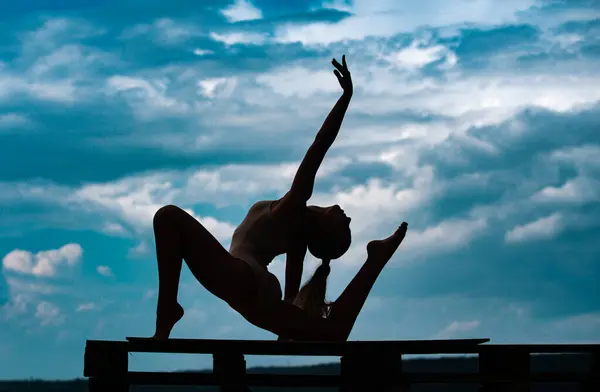 Yoga woman stretching with pose stretch. Silhouette of fit fitness athlete girl exercising sports stretches. Cloudy sky background