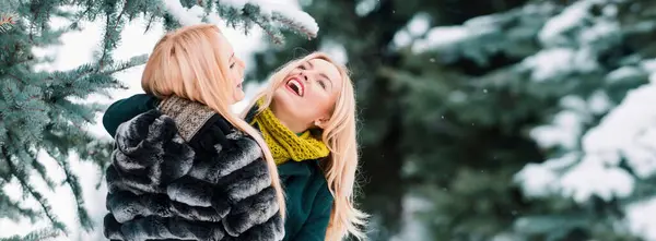Winter woman friends laughing on winter snowy background outdoor. Portrait of young beautiful women couple having fun. Models walking in winter street. Female winter fashion concept