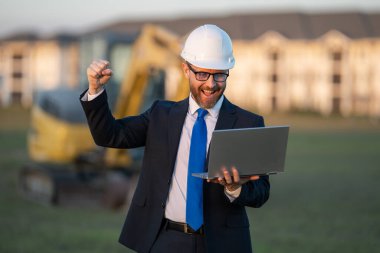 Başarılı bir inşaat işletmesi sahibi. Kazıcının yanındaki kask ve takım elbiseli inşaat işçisi. İnşaat alanının önünde kendine güvenen bir inşaat sahibi. İnşaat mühendisi.