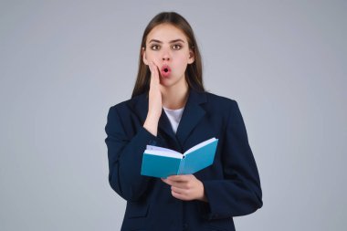 Elinde not defteri olan takım elbiseli genç bir kadın, gri arka planda izole edilmiş. Not defteri olan bir öğrenci. Not defteri düzenleyicisi olan sürpriz öğrenci. Genç iş kadını not defterine yazıyor.