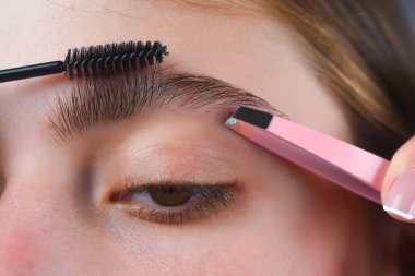 Mükemmel bir kaş. Kadının kaş makyajı yaptırmasına yakın çekim. Makro kaşına fırçayla kozmetik uyguluyordu. Mükemmel bir kaş şekli, kahverengi göz farı ve uzun kirpikleri. Şekli kaşlar