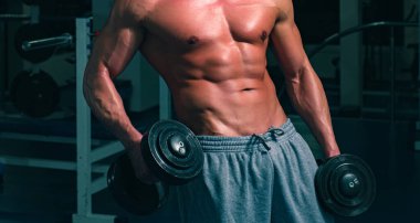 Çıplak karın kasları. Spor salonundaki sporcu. Çıplak gövdeli sportif bir erkek. Antrenman adamı. Dambıllı egzersizler. Güçlü atletik vücut