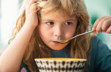 Evde kahvaltı yapan çocuk portresi. Küçük tatlı bir çocuğun portresi. Sarı saçlı. Tabak kaşığı yiyor.