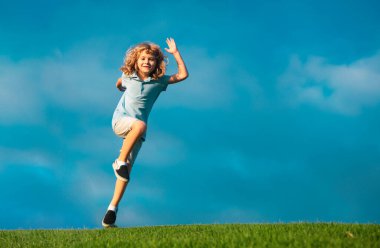 Little adorable boy running on grass. Excited kid play the green grass. The child has blond long hair and a t-shit. The concept of harmony with nature and care for ecology. Healthy lifestyle