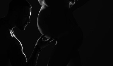 Siluet portresi koca hamile kadının göbeğini öpüyor. Anne ve baba bebek sevgisi kavramını bekliyor. Mutlu genç çift bebek bekliyor. Siyah arka planda izole edilmiş.