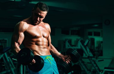 Spor salonunda pazı kaldıran bir sporcu. Spor salonunda egzersiz yapan kaslı bir adam. Güçlü erkek, çıplak karın kasları.