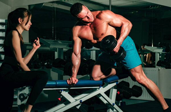 Trainer dumbbell exercises. Boodybuilder couple. Personal friend helping woman working with heavy dumbbells in gym. Sportsman concept. Sport woman