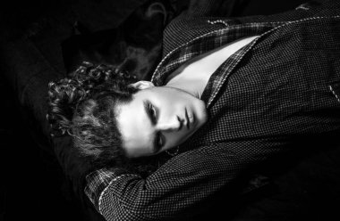 Ciddi yüzlü ve vahşi bir tarzı olan bir adam. Kıvırcık saçlı, kendine güvenen bir adam. Siyah arka planda izole edilmiş ve kameraya bakıyor. Berber dükkanı reklamı.