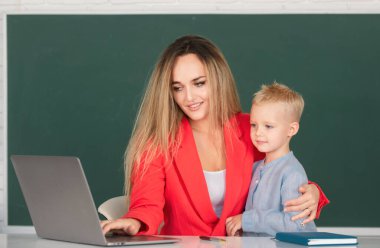 Anne ve oğlu birlikte bilgisayar laptopu kullanıyorlar. Okul çocuğu çevrimiçi eğitim öğreniyor. Öğretmen okul çocuğuna dersi açıklıyor. İlkokul öğrencileri öğreniyor. Anne ve oğul öğreniyor.