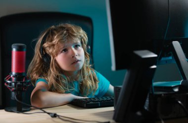 Küçük bir çocuk geceleri masaüstü kullanıyor. Neon yıldırımlı odada bilgisayar ekranı olan bir çocuk. Klavyede yazarken sevimli çocuğun portresi