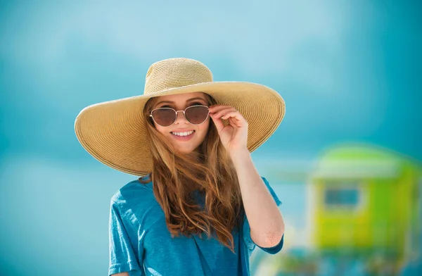 Close-up portrait of smiling woman by the sea. Happy woman in sunglasses and straw hat standing at the seaside