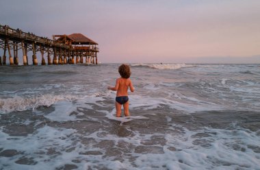 Çocuk dışarıda eğleniyor. Denizde tatiller, komik çocuklar, okyanus sahilinde oynayan çocuklar. Çocuk mavi denizde dalgalarla oynuyor. Seyahat ve macera konsepti
