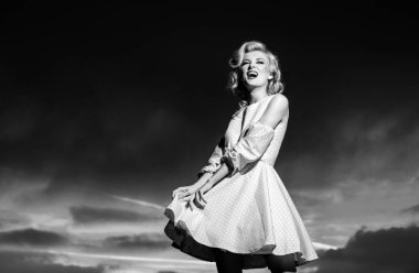 Monroe elbiseli kadın dramatik bir gökyüzünde. Moda kadını dışarıda poz veriyor. Seksi elbiseli çekici genç kadın yazın tadını çıkarıyor.