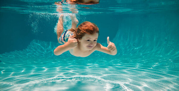 Underwater child swim in water swimming pool. Summer activity and healthy kids lifestyle. Summer vacation with children in a tropical resort. Kid boy with thumbs up under water