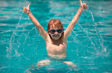 Parmağını kaldırmış yüzme havuzunda yüzen çocuk. Suyun içine su sıçratır, boş zamanlarında kollarını açarsın.