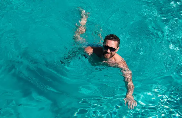 Man at summer vacation. Guy in sunglasses swimming in pool. Summertime pool resort