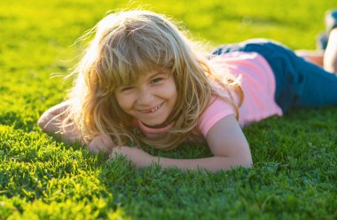 Bahar çocuğu suratı. Çimen geçmişi olan gülümseyen çocuk. Yaz parkında küçük mutlu bir çocuğun portresi.