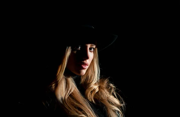 Sexy gorgeous woman with shadows on beautiful face and fashion hat on black studio. Fashion portrait of beautiful woman with dark light on face