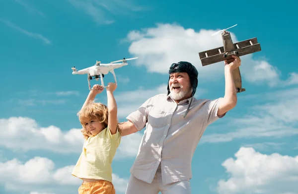 Grandson child and grandfather hold plane and drone quad copter against sky. Child pilot aviator with plane dreams of flying. Family Relationship Grandfather and child