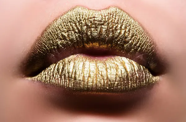 Gold lips. Woman wouth close up with golden color lipstick on lip. Glitter glossy lips biting