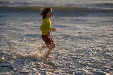 Denizde koşan kaygısız çocuk. Sıcak bir yaz gününde okyanus kenarında koşan mutlu şirin çocuk. Aile tatilinde okyanusta ya da denizde koşup sıçrayan sevimli küçük bir çocuk. Çocuk sahilde koşuyor.