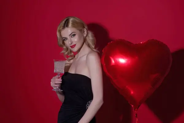 Young beautiful sexy woman drink champagne. Love and valentine beauty girl. Sexy girl holding heart shape balloon. Sexy woman hold red heart symbol of Valentines day and love