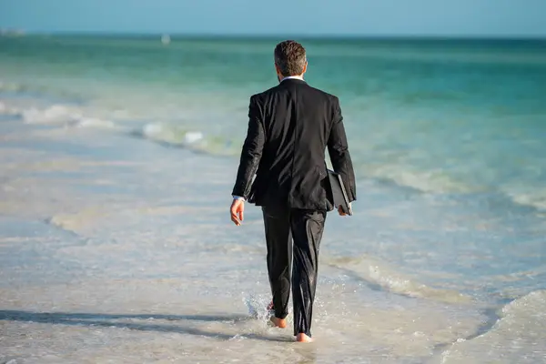 Funny business man in suit on sea. Rear view of back business man in suit in sea water at beach. Business man remote on-line working. Dream for summer vacations office workers