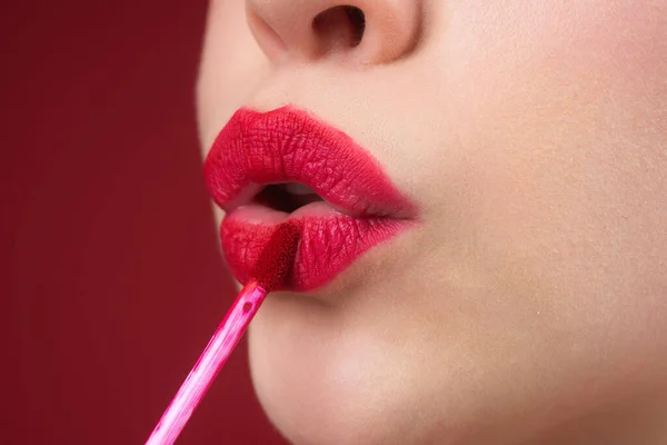 Applying lipstick. Painting lips with bright lipstick, close up. Pampering, lips correction concept. Glossy lipstick on full plump lip. Woman hand applying lipstick