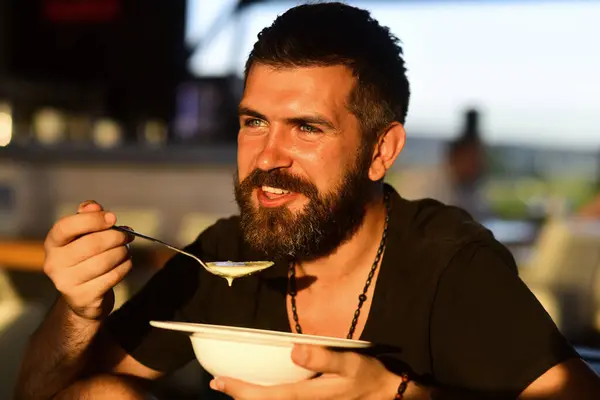 Man eat soup. Good Appetite. Bearded man with bowl of soup. Happy guy eating soup outdoor. Man eating delicious soup in restaurant. Dinner and meal. Man eating lunch in a cafe