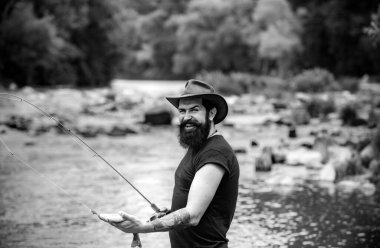 Alabalık yakalayan hippi sakallı adam. Genç adam balık tutuyor. Çubuklu balıkçı, nehir kıyısında dönen makara. Adam balık yakalıyor, gölde balık tutarken olta çekiyor. Vahşi doğa.