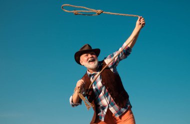 Vahşi batı kovboyu rodeoda. Kementle bağlanmış batı emeklisi. Sakallı, kahverengi ceketli, şapkalı, at ya da inek yakalayan adam.