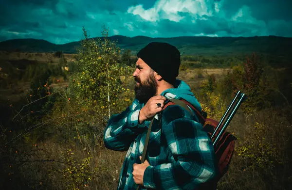 Mountain hunting. Hunter with shotgun gun on hunt. Bearded hunter man holding gun and walking in forest