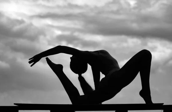Silhouette of female fit model on loudy sky background. Stretching and motivation. Woman gymnast, gymnastics acrobat