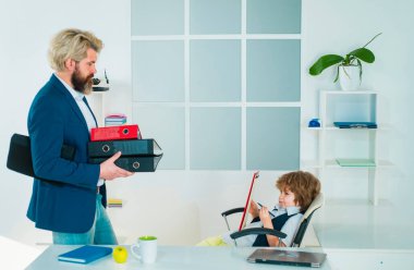 Patron ve iş adamı ofiste birlikte çalışıyorlar. Ofisteki bir iş masasında patronluk taslayan küçük çocuk.