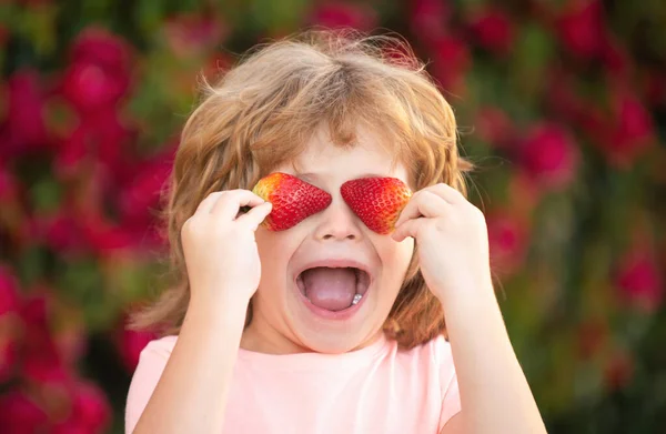 Child fun with strawberries. Happy funny child holding strawberries in the summer outdoor