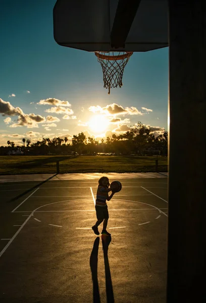 Cute smiling boy plays basketball. Active kids enjoying outdoor game with basket ball. Sport for kids