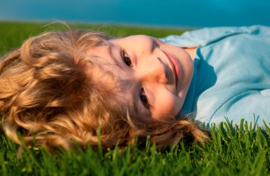 Yeşil çimlerin üzerinde yatan gülümseyen küçük bir çocuğun portresi. Gülümseyen çocuk bahar bahçesinde eğleniyor.